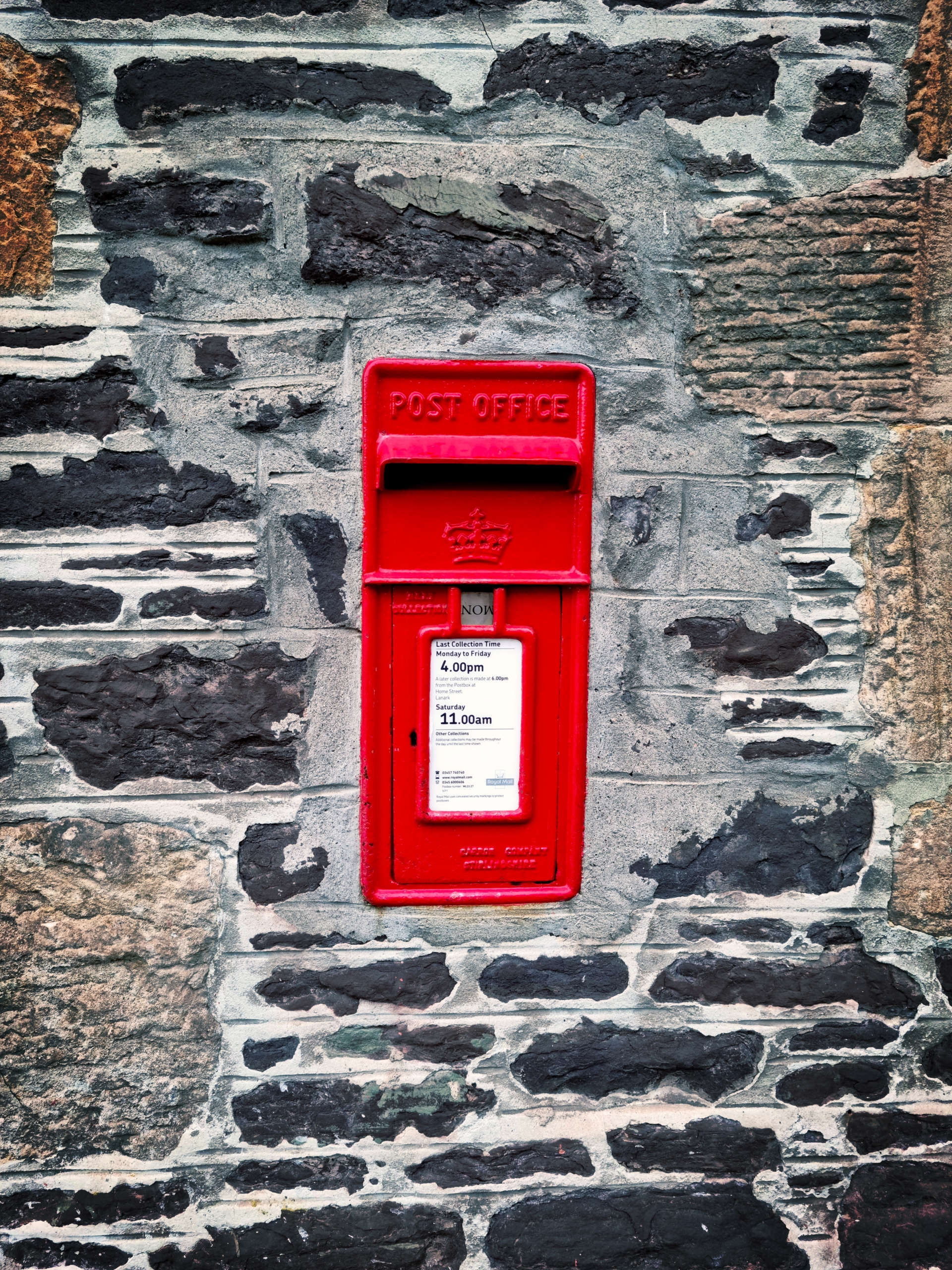 red mail box mounted on gray brick wall